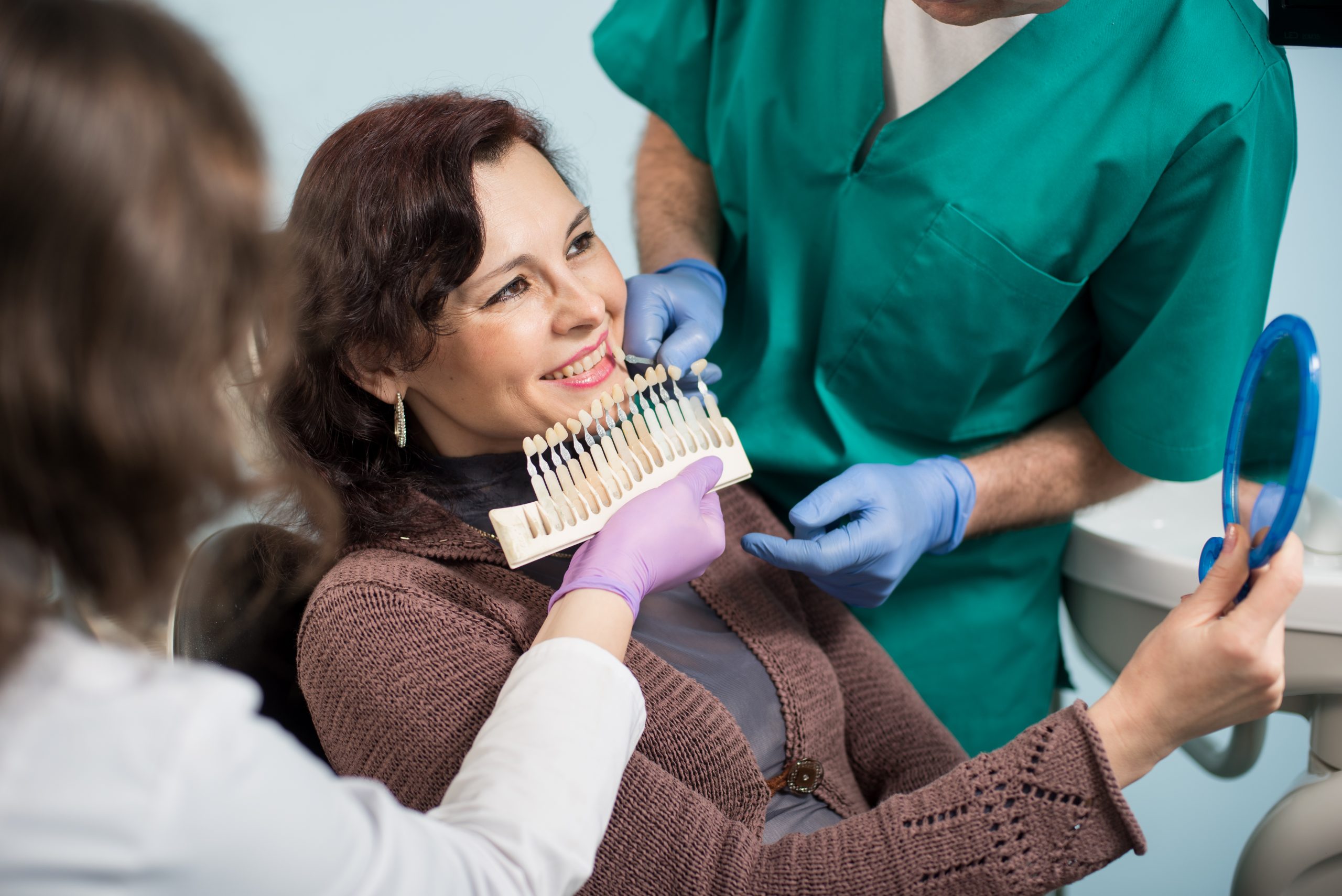 Dentist with assistant checking and selecting colour of the teeth in dental clinic office